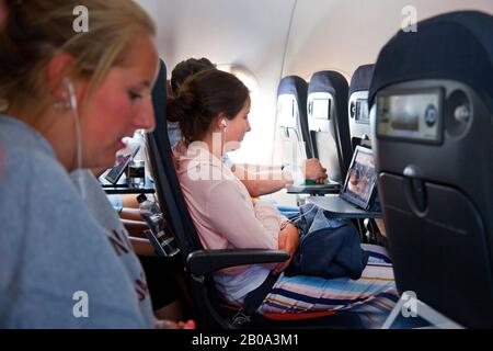 Adolescentes ( les deux modèles relâchés ) assis sur un avion Easyjet portant un casque et regardant des appareils portables ( ipad ) pendant le vol. Banque D'Images