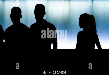 Silhouettes de deux garçons adolescents et une fille marchant devant un bâtiment moderne, dans une nuit à contraste élevé Banque D'Images