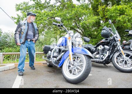 MCC Biker MAN avec casquette noire marche autour de la moto haute à Harley-Davidson Reading Berkshire Angleterre Banque D'Images