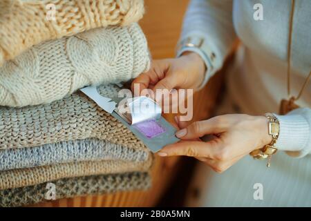 Gros plan sur la jeune femme en sweat blanc et jupe assis près du canapé avec tas de chandails et à l'aide d'un tissu anti-moth lavande garde-robe répulsif à m Banque D'Images