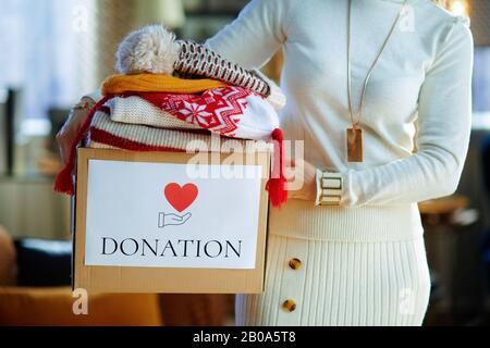 Gros plan sur une femme branchée en sweat blanc et jupe avec boîte de donation avec vieux vêtements chauds à la maison moderne en hiver ensoleillé. Banque D'Images