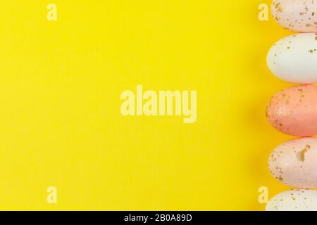 Des œufs peints de façon créative dans des tons pastel décorés de feuilles d'or sont disposés en rangée le long du bord latéral sur fond jaune, espace de copie. Joyeuses Pâques D. Banque D'Images