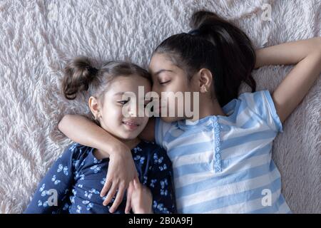 Deux jeunes filles noires, sœurs, se trouvent au lit dans une embrasse sur le dos. Des filles persanes sur le lit avec un téléphone. Enfants du Moyen-Orient. Banque D'Images