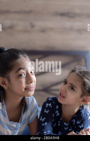 Deux jeunes filles à peau foncée, sœurs, se trouvent au lit et montrent des émotions tristes et gaies. Des filles persanes sur le lit avec un téléphone. Enfants du Moyen-Orient. Banque D'Images