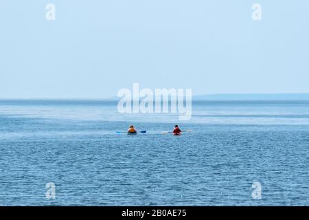 Deux kayaks se sont dirigés vers la mer pour une journée lumineuse mais hazy. Les gens ne sont pas identifiables et portent des gilets de sauvetage. . L'océan est bleu clair. Banque D'Images