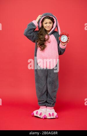 Alarme du matin. Bunny rouge enfant fond. Bébé animal. Temps de comptage. Jour normal de début. Adorable réveil à motif lapin. Petite fille en costume de lapin. Enfant lapin kigurumi. Pyjama fille à motif lapin. Banque D'Images