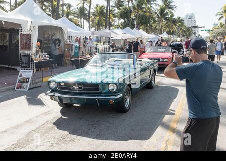 Un touriste prend une photo d'une voiture Ford Mustang convertible d'époque exposée pendant le week-end Art déco à Miami Beach, aux États-Unis Banque D'Images