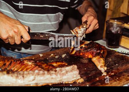 Le chef coupe le porc grillé dans des steaks avec couteau. Cochon de succion traditionnel cuit sur le gril à charbon. Le petit cochon est grillé dans son ensemble sur un o Banque D'Images