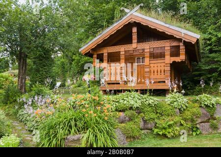 La façade de la maison de jeu des enfants en pin taché de brun doré est ornée de détails en bois sculpté et de Gramineae ou de Poaceae - Graminées et Bryophyta - Moss verts. Banque D'Images