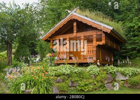 La façade de la maison de jeu des enfants en pin taché de brun doré est ornée de détails en bois sculpté et de Gramineae ou de Poaceae - Graminées et Bryophyta - Moss verts. Banque D'Images