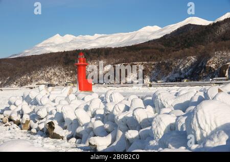 JAPON, ÎLE D'HOKKAIDO, PÉNINSULE DE SHIRETOKO , PORT D'UTORO, PHARE ROUGE AVEC MONTAGNES EN ARRIÈRE-PLAN Banque D'Images