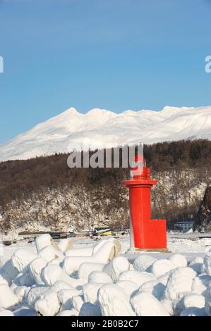 JAPON, ÎLE D'HOKKAIDO, PÉNINSULE DE SHIRETOKO , PORT D'UTORO, PHARE ROUGE AVEC MONTAGNES EN ARRIÈRE-PLAN Banque D'Images