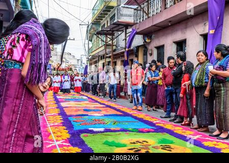 Santiago Atitlan, Guatemala - 19 avril 2019: Traditionnellement habillés locaux mayas regarder Le Vendredi Saint procession approche sur le tapis de sciure de bois teint. Banque D'Images