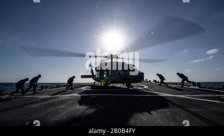 200213-N-TI693-1146 GOLFE ARABIQUE (FÉV 13, 2020) - Les Marins affectés au destroyer de missile guidé USS Carney (DDG 64) sont en position de retirer les cales et les chaînes d'un hélicoptère Sea Hawk MH-60 pendant les opérations de vol, 13 février 2020. Carney est déployé dans la 5ème zone d'opérations de la flotte des États-Unis à l'appui des opérations navales pour assurer la stabilité et la sécurité maritimes dans la région centrale, reliant la Méditerranée et le Pacifique à travers l'océan Indien occidental et trois points stratégiques de starter. (ÉTATS-UNIS Photo marine par Spécialiste Communication de masse 1ère classe Fred Gray IV) Banque D'Images