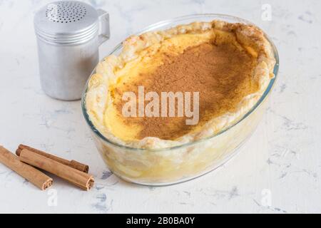 Tarte au lait rustique sur la surface de la cuisine avec bâtonnets de cannelle et shaker à la cannelle - photo sélective du dessert traditionnel sud-africain Banque D'Images