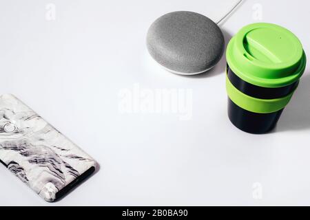 Concept d'assistant numérique. Enceinte plate avec éclairage LED activée avec smartphone court, bloc-notes vert, stylo et tasse à café réutilisable. Banque D'Images