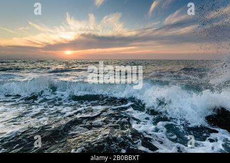 Une vague roule à la ligne de rivage alors que le soleil se couche à l'horizon de l'océan. Banque D'Images