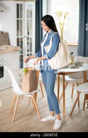 Jeune femme debout dans le sac de cuisine sur chaise. Banque D'Images