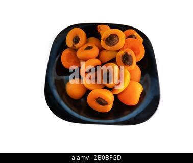 Moitiés d'abricots avec de la pierre noire sur une assiette. Le contraste des couleurs. Isoler sur fond blanc Banque D'Images