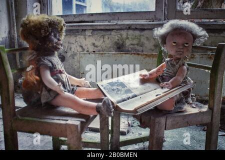 Poupées à la crêpe sur des chaises de jouet avec un livre dans un bâtiment abandonné à Pripyat, en Ukraine, site du déaster nucléaire de Tchernobyl en 1986. Banque D'Images