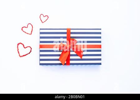 Boîte à rayures bleu cadeau avec noeud en satin rouge et trois coeurs peints. Isolé sur le fond blanc. Concept de jour de vacances et de valentines. Banque D'Images