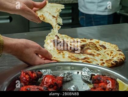 Un pain naan fraîchement préparé est retiré prêt à manger. Au premier plan, du poulet cuit tandoori sur une plaque. Banque D'Images