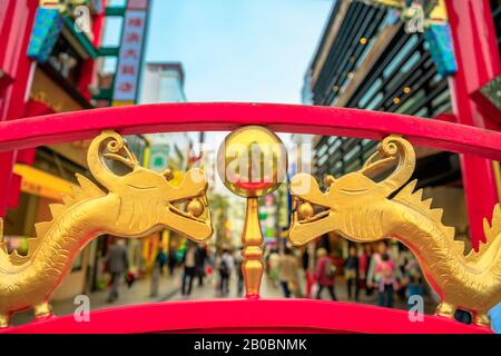 Détails des dragons dorés chinois sur l'une des portes du quartier chinois de Yokohama au Japon avec des gens marchant dans une ville étroite sur le backgroung flou. Banque D'Images