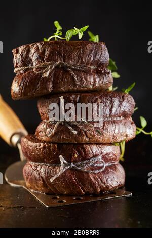 Médaillons de bifteck de filet grillé attachés à la ficelle et garnis avec des herbes fraîches empilées sur une spatule en métal dans une vue latérale rapprochée Banque D'Images