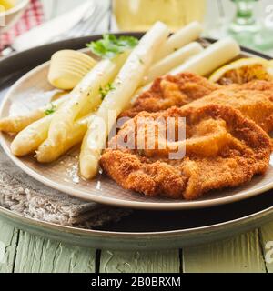 Les asperges blanches en conserve épient avec du poisson frit pané doré, des herbes fraîches et un beurre se recourent près d'une assiette servie sur un plateau Banque D'Images