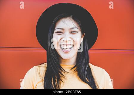 Portrait d'une heureuse fille asiatique souriant avec un arrière-plan corail - jeune femme chinoise qui s'amuse se posant devant l'appareil photo - mode, vêtements décontractés an Banque D'Images