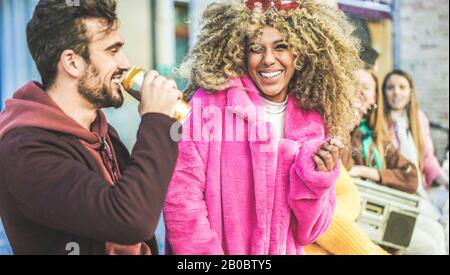 Des gens à la mode issus de diverses cultures font la fête en plein air pour boire de la bière, fumer et écouter de la musique - les jeunes amis s'amusent le week-end soir - Banque D'Images