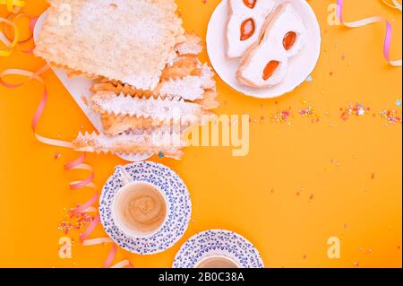 Crostoli, chiacchiere, biscuits et espresso parfumé sur un fond jaune, coloré avec des confettis et décor festif. Café et bonbons pour un carnaval italien traditionnel à Viareggio. Banque D'Images