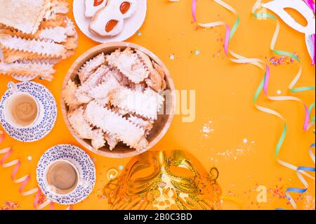 Crostoli, chiacchiere, biscuits et espresso parfumé sur un fond jaune, coloré avec des confettis et décor festif. Café et bonbons pour un carnaval italien traditionnel. Pose plate. Espace de copie Banque D'Images