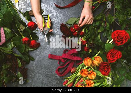 Une femme recueille un bouquet de fleurs printanières sur une table en pierre. Fleuriste en milieu de travail. Banque D'Images