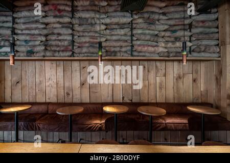 Café dans un style loft avec des murs en bois texturés. Il y a des tables rondes avec des canapés et des chaises, de nombreux sacs à grain, des lampes lumineuses suspendues. Horizo Banque D'Images