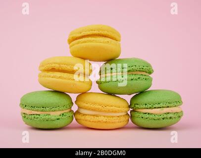 une pile de macarons de gâteaux de farine d'amande ronde jaune et verte avec de la crème sur un fond rose, un délicieux gâteau Banque D'Images