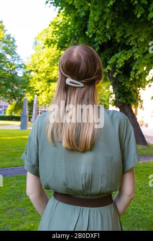 Vue arrière jeune fille avec cheveux blond et belles perles coiffure et robe d'olive dans le parc. Banque D'Images