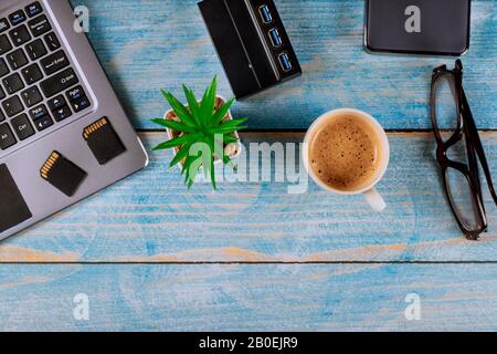 Mélange de photographes de bureau et de gadgets travaillant sur un ordinateur portable dans une tasse de café sur disque dur externe et lecteur USB3.0 de cartes SD mémoire Banque D'Images