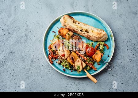 Savoureuses kebabs de légumes barbecue avec tofu, citrouille ou noyer, tomate et champignons sur un lit de salade verte servi sur une plaque bleue en hauteur Banque D'Images