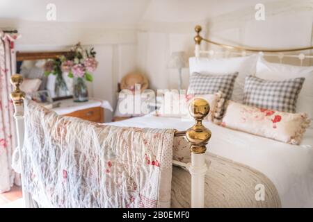 Patchwork quilt de Debbie En Duvet fait de restes de tissus favoris, sur un lit en fer forgé coussins Vichy et roses rouges sur un lit en fer forgé Banque D'Images