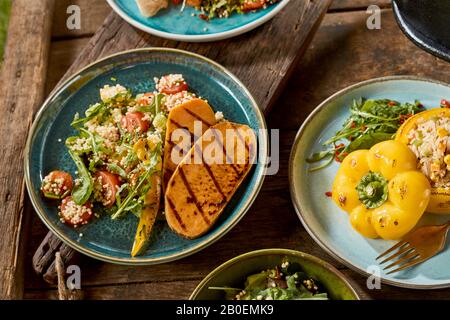 Patate douce grillée sur un lit de salade de quinoa avec des légumes verts et des tomates servis avec du poivron et du couscous farcis dans une vue en haut sur un bois rustique Banque D'Images