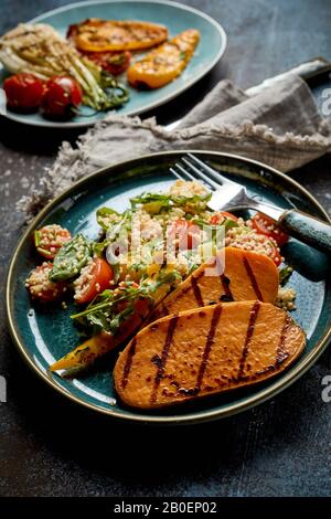 Tranches de pommes de terre douces fraîches grillées ou barbecue servies avec une délicieuse roquette et une salade de céréales pour un barbecue végétalien et végétarien sain sur une assiette avec des utens Banque D'Images