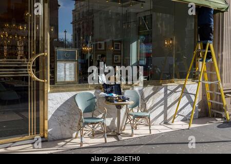 Alors qu'un serveur sert des clients assis en hiver au soleil, un ouvrier se tient sur des escabeaux pour réparer l'auvent de Cafe Grand par Concerto à l'angle de Douvres Street et Piccadilly, le 18 février 2020, à Londres, en Angleterre. Banque D'Images