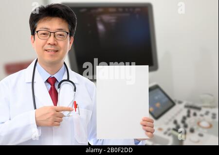 Médecin homme tenant une carte de messages devant un dispositif de diagnostic par ultrasons Banque D'Images