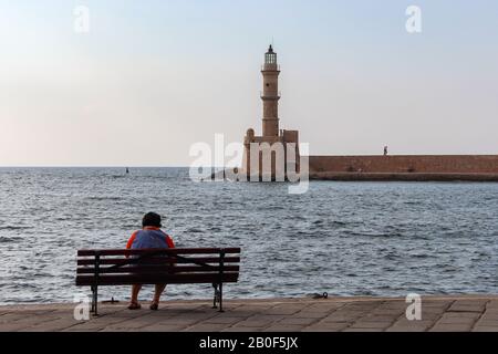 Une femme solitaire assise sur un banc dans le vieux port de la Canée, Crète et regardant le vieux phare Banque D'Images