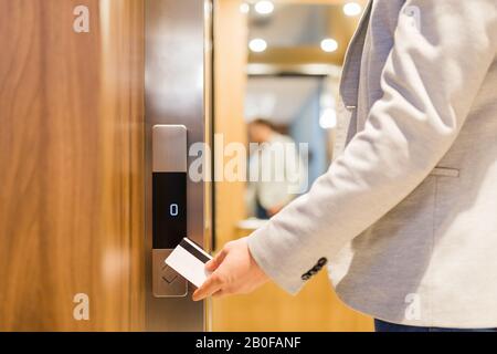 Homme tenant la carte-clé sur le capteur pour ouvrir la porte de l'ascenseur dans le bâtiment moderne ou l'hôtel. Banque D'Images