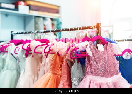 Rack avec de nombreuses belles robes de vacances sur des cintres à la mode femme salle d'exposition intérieure. Enfant fille robe louer studio pour anniversaire de célébration Banque D'Images