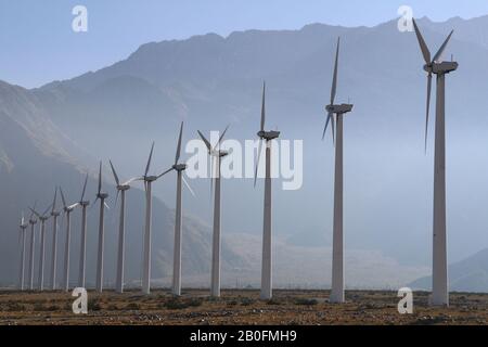 un après-midi brumeux dans le désert avec des montagnes et une rangée de grandes éoliennes Banque D'Images
