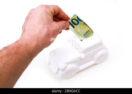 La main entre un billet dans la boîte à monnaie en forme de voiture en céramique. Elle peut être le symbole des coûts des réparations, des investissements, des économies ou de l'assurance de la voiture. Banque D'Images