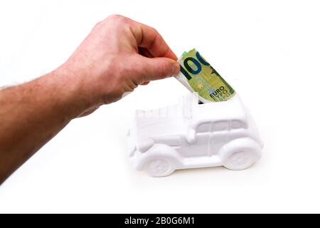 La main entre un billet dans la boîte à monnaie en forme de voiture en céramique. Elle peut être le symbole des coûts des réparations, des investissements, des économies ou de l'assurance de la voiture. Banque D'Images